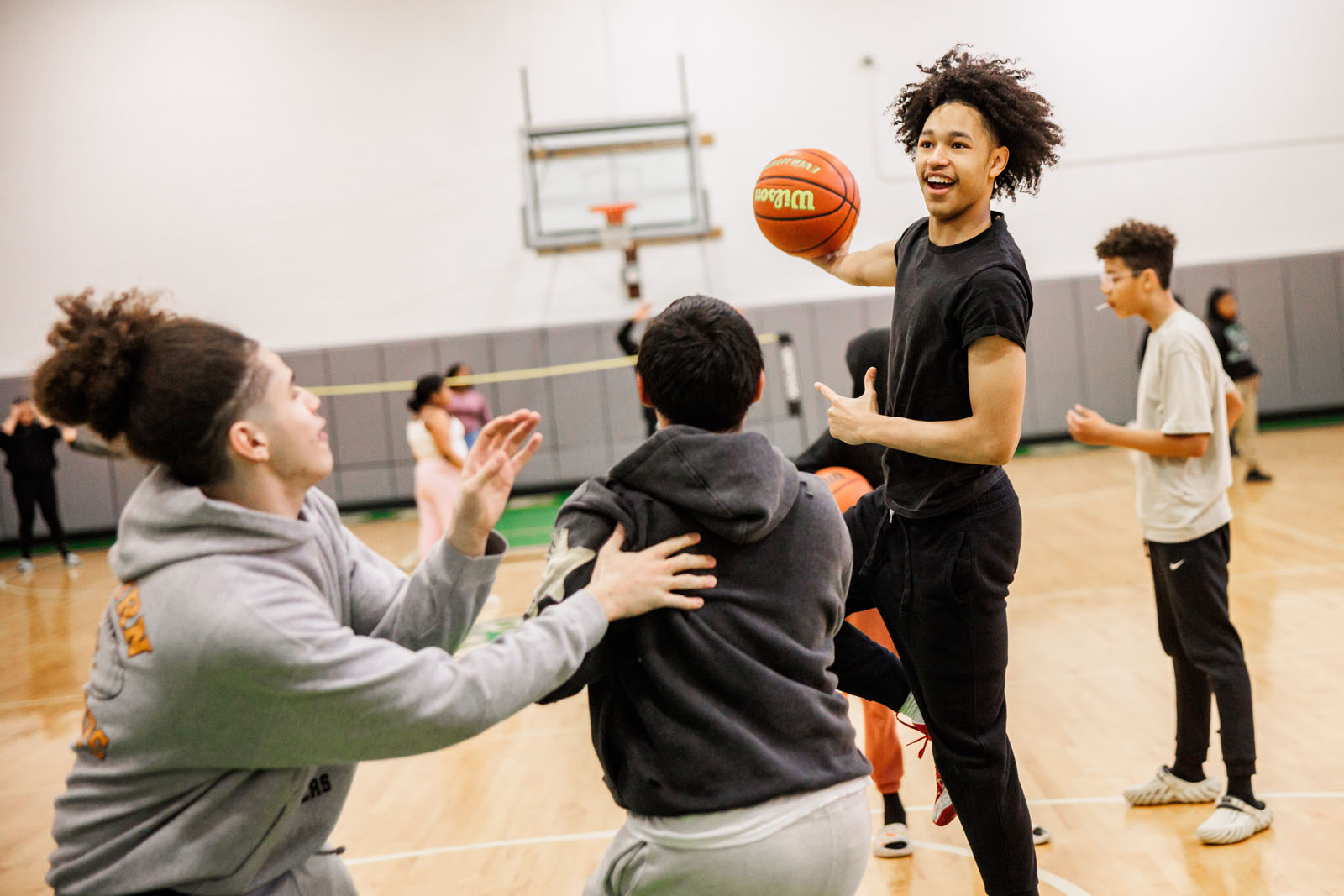 A focused shot captures three teens in the midst of playing basketball, one of them holds the basketball, while the others move with purpose around him.